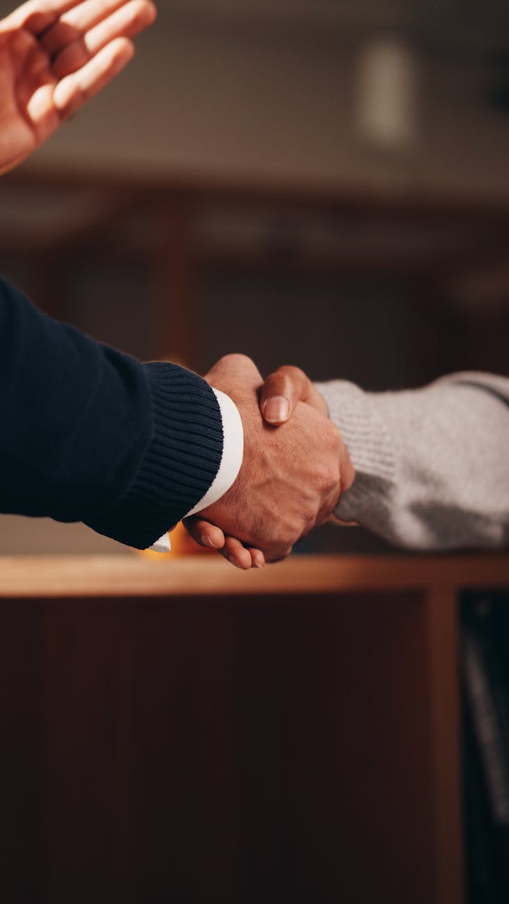 Two professionals shaking hands over business documents on a desk, symbolizing an agreement.